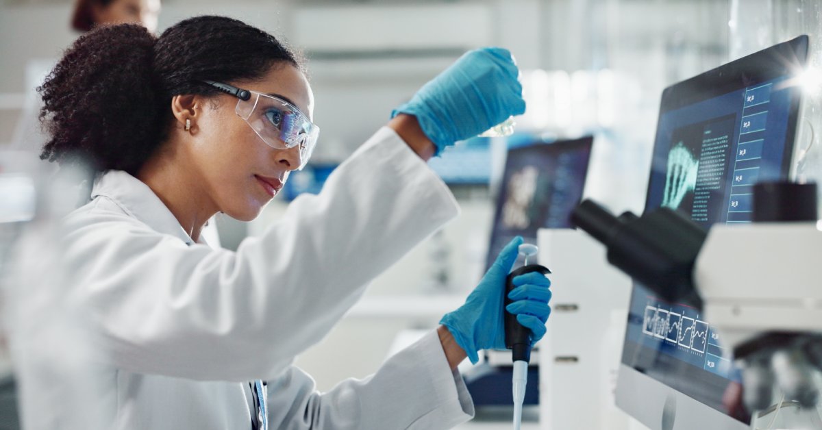 A health-care professional wearing protective glasses and a white lab coat, holding an instrument in her left hand.