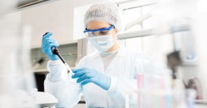 A health-care professional wearing protective glasses and a facemask, holding a black object in her right hand.