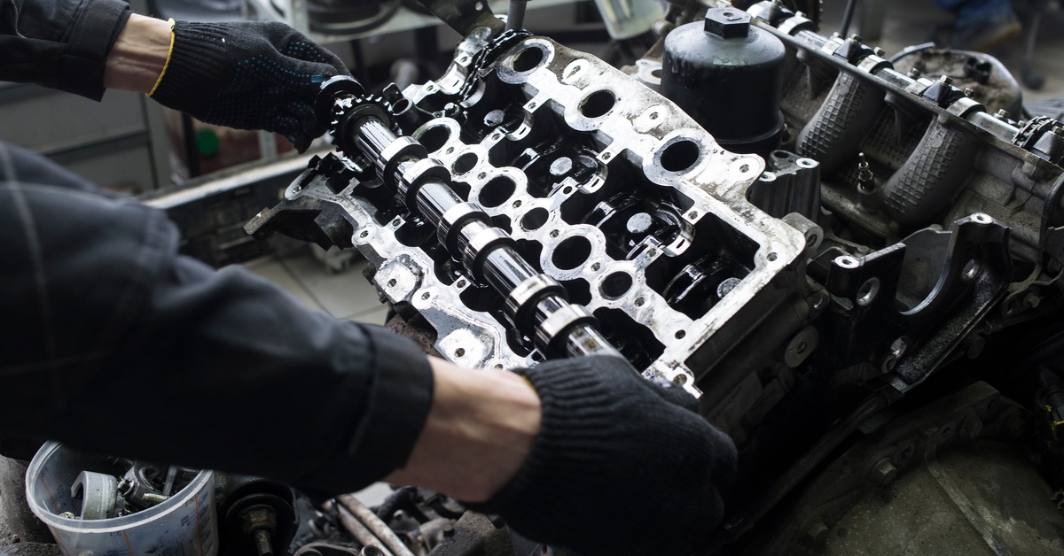 A person is wearing gloves while handling an engine. There is a bucket filled with parts on the ground next to the person.