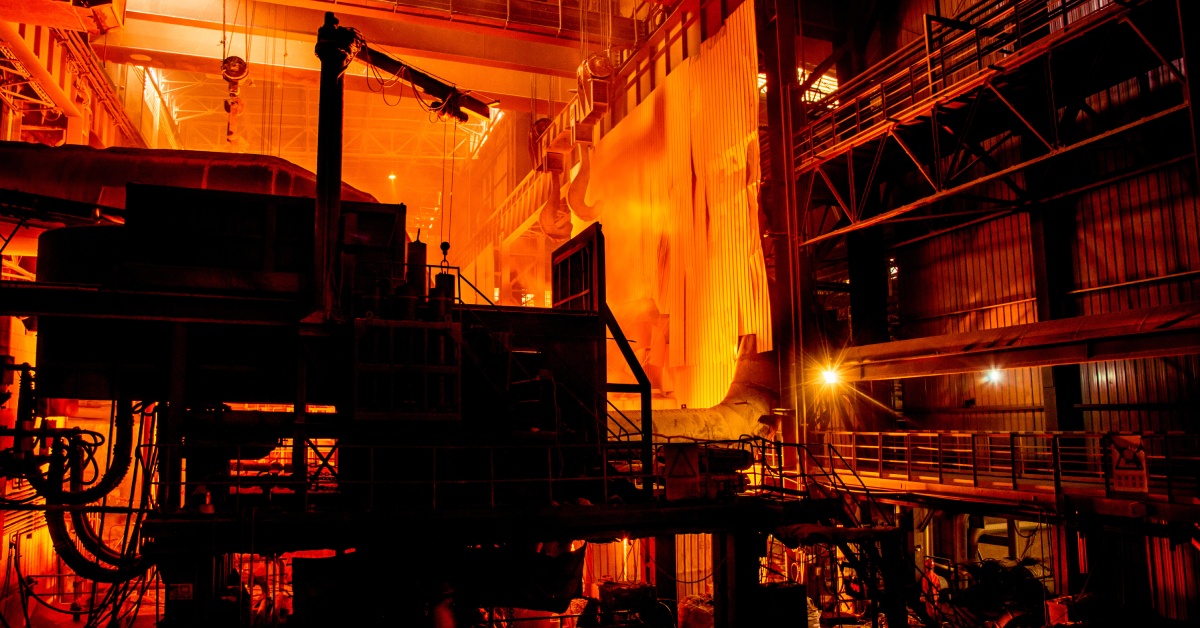 A facility aglow with orange light. There are walkways to the right and cranes attached to the ceiling.