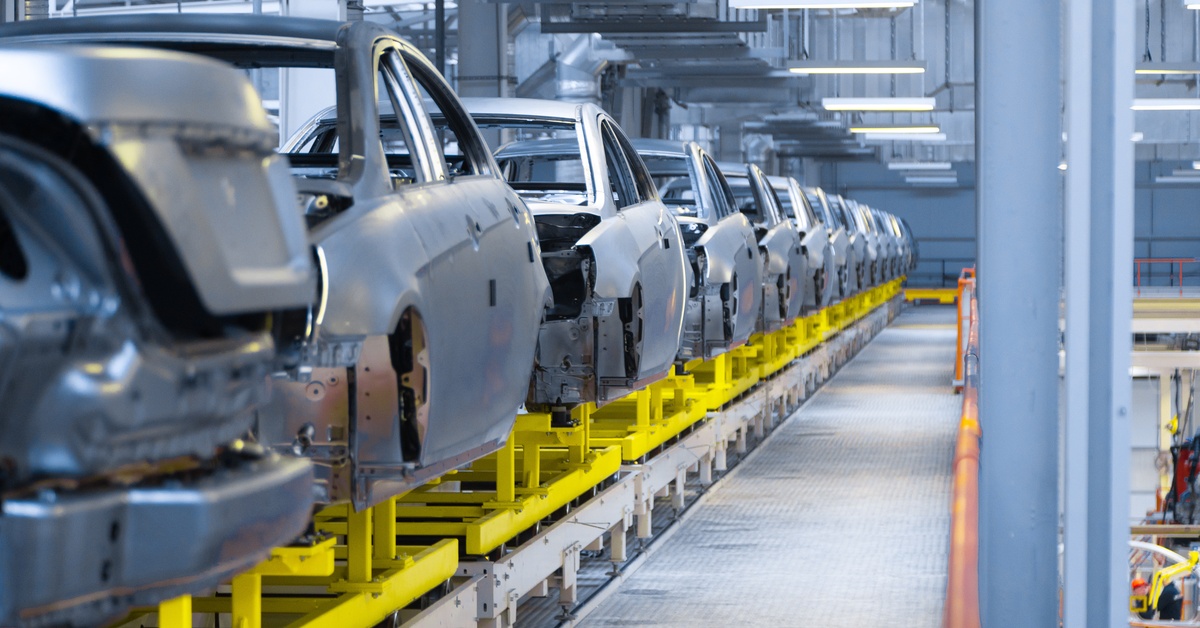 Several half-made car bodies are in a line. They are in a facility and each body is resting on a yellow surface.