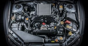 A car has its hood open and its engine is exposed. There are many mechanical parts and the car is gray in color.