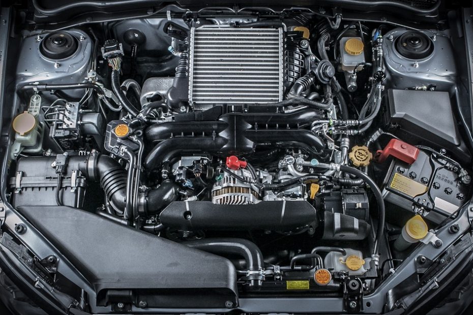 A car has its hood open and its engine is exposed. There are many mechanical parts and the car is gray in color.