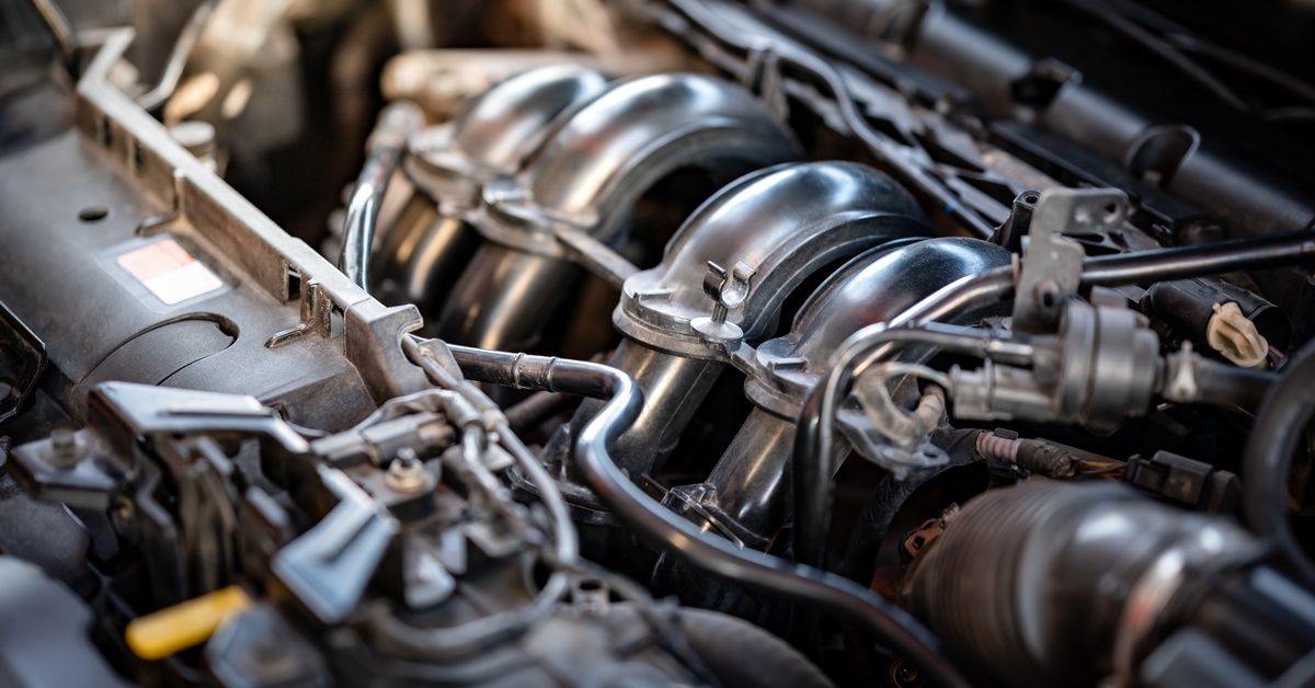Automotive components inside a car engine. Most of the parts are steely-gray, while others are black rubber.