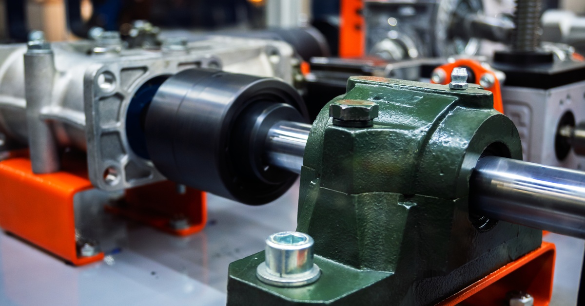 A piece of heavy machinery in the middle of a factory setting. Some components are painted green.