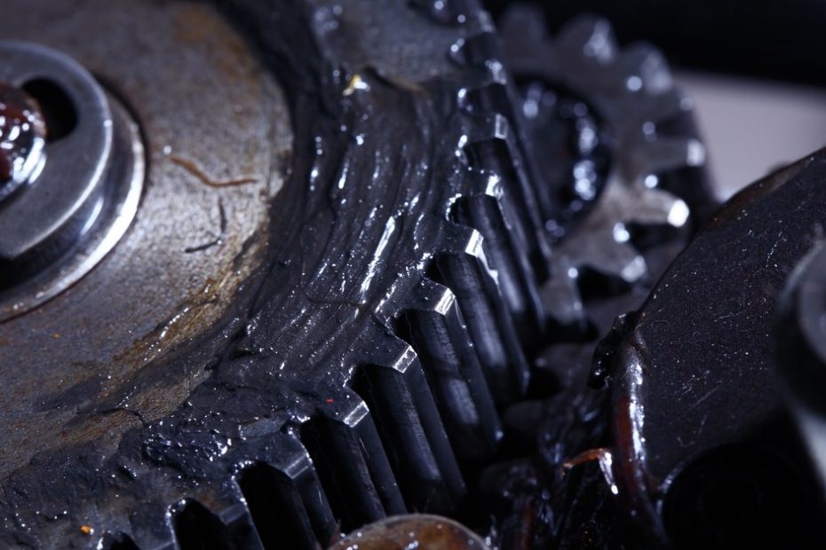 A metal gear with a screw in the middle is covered in a slick substance. There is another gear behind it.