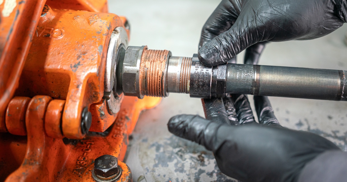 There is an orange piece of machinery and a person is holding a part of it with both hands.