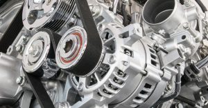 The machinery of a vehicle engine. There are many silvery parts along with several rubber belts.