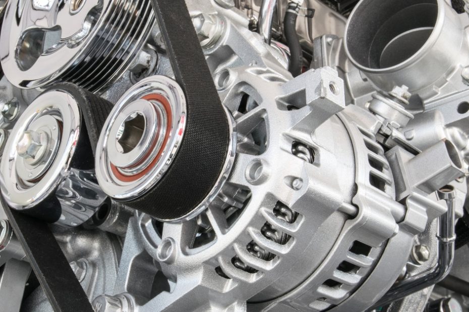 The machinery of a vehicle engine. There are many silvery parts along with several rubber belts.