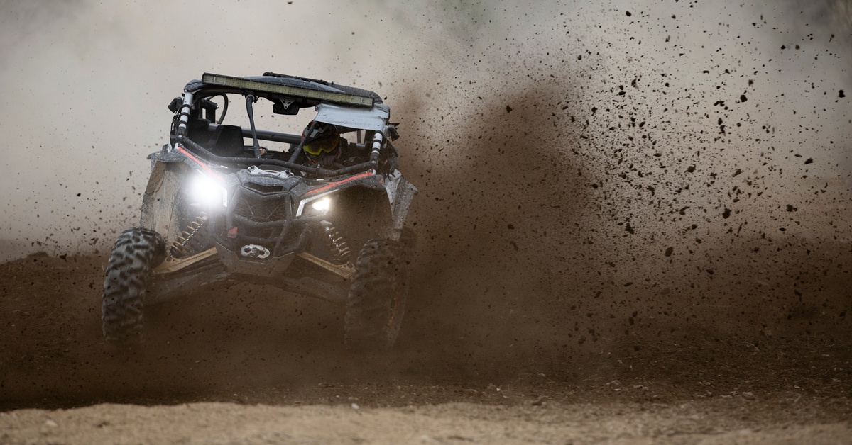 A car is driving through a cloud of dirt that has been kicked up. The car’s headlights are on.