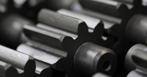 A person is in an industrial workshop. He is inspecting a piece of machinery with a precision tool.