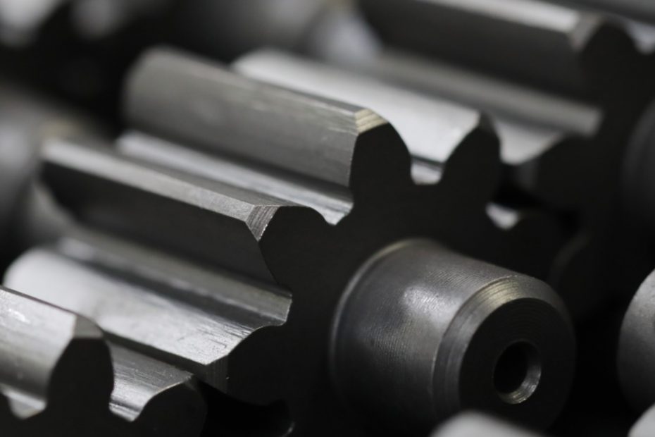 A person is in an industrial workshop. He is inspecting a piece of machinery with a precision tool.