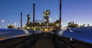 An oil and gas complex is in the background during the night. There are pipes running to the complex.