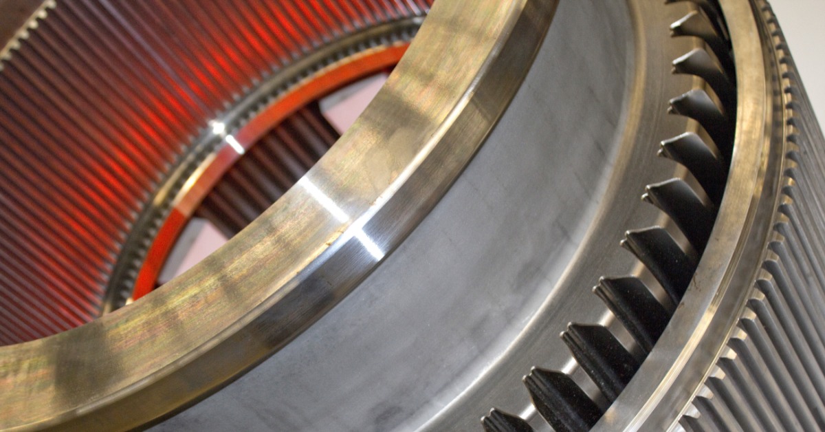 A large, circular metal object has teeth cut into it. There is orange reflected in the metal.