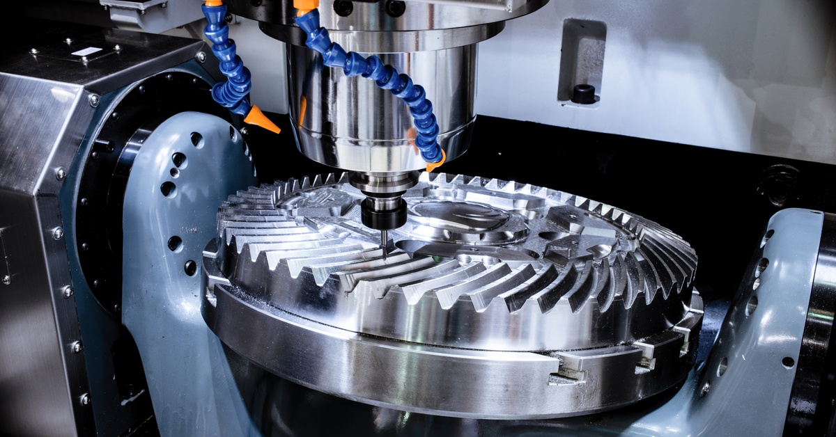 A circular piece of metal is sitting on another metal surface. There is a CNC machine cutting out a design on the metal.