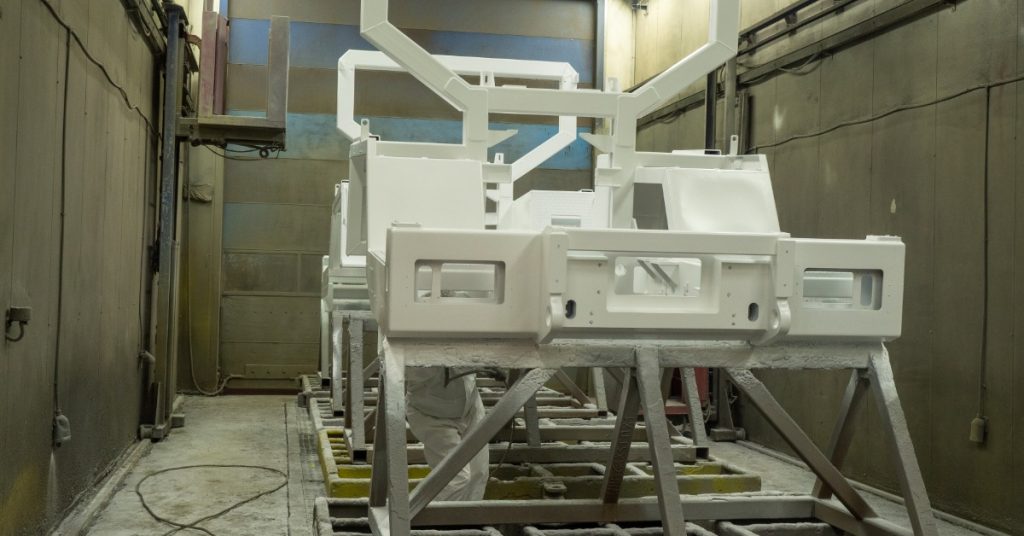 Several pieces of metal are sprayed white. They’re all standing up straight on a holder contraption.