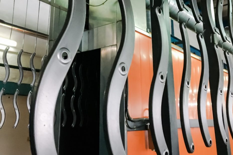 There are numerous curved metal pieces that are suspended from a rack. There is an orange wall in the background.