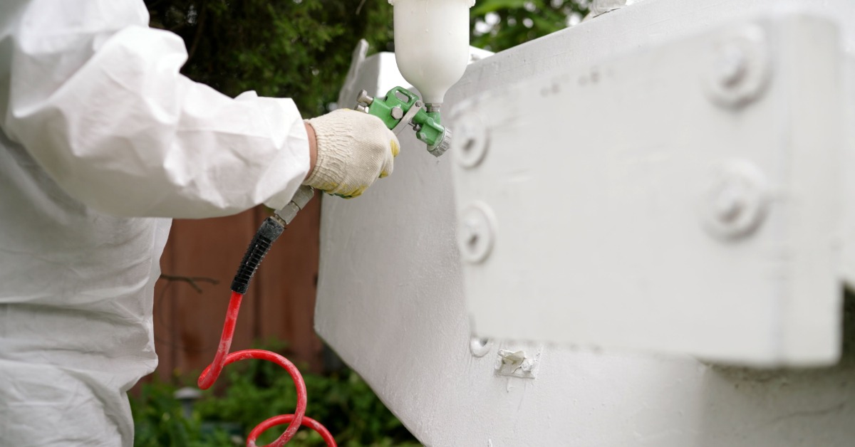 A person in white is using a hose to spray a white metal object. The man and object are in an outdoor environment.