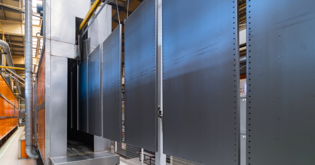 A line of metal slabs are hanging from a conveyor system. They are in a warehouse environment.