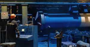 A person in an orange hard hat is standing next to heavy machinery that is painted blue.