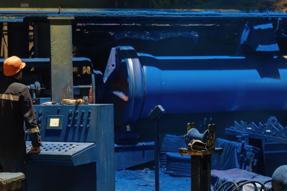 A person in an orange hard hat is standing next to heavy machinery that is painted blue.