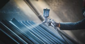 A person is using a spray gun to spray down several pieces of metal. The spray has a bluish tint to it.