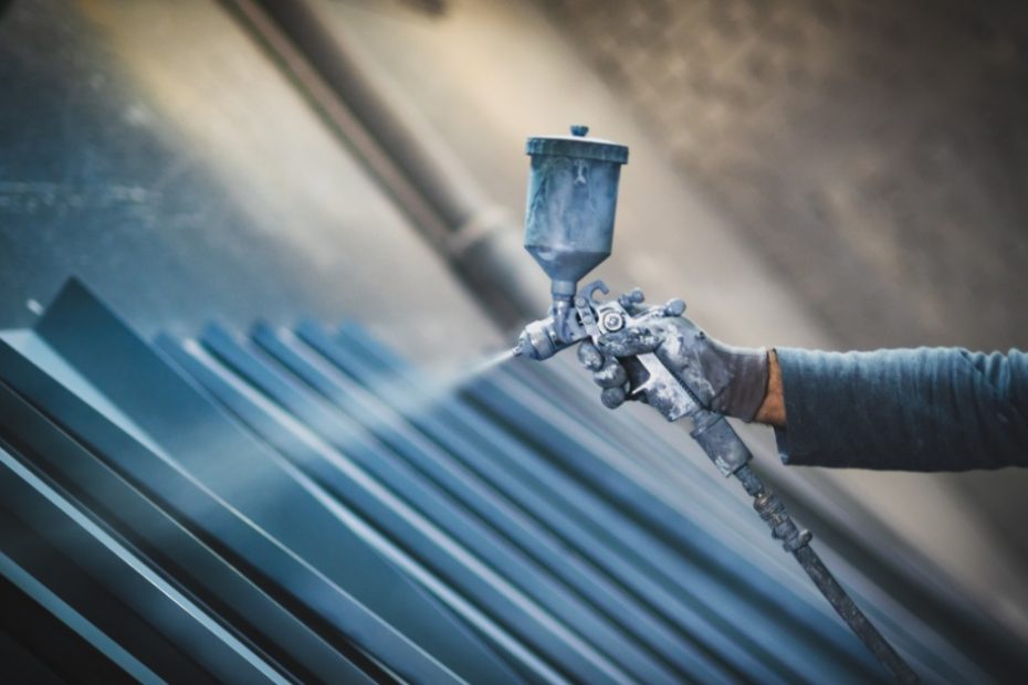 A person is using a spray gun to spray down several pieces of metal. The spray has a bluish tint to it.
