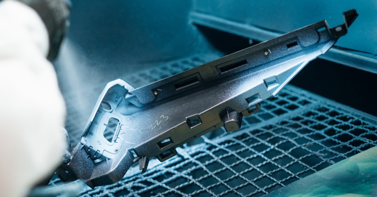 A piece of metal is sitting on a grated surface. A person is holding a spray gun and shooting some type of spray at the metal.