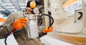 A man in protective wear is using a spray nozzle to spray pieces of metal with a type of coating.