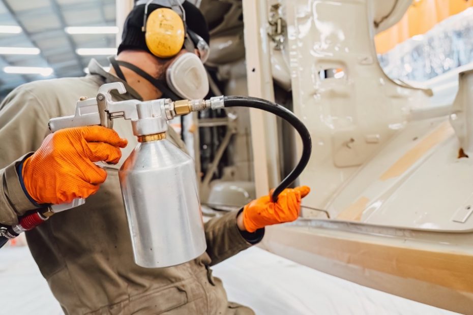 A man in protective wear is using a spray nozzle to spray pieces of metal with a type of coating.