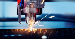 An industrial machine is sparking against a sheet of metal. The background is a dark blue.