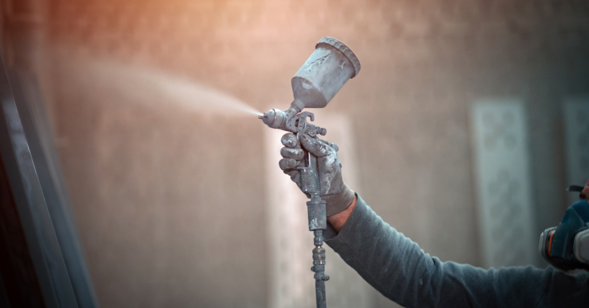 A person is holding a spray gun in their hand. They are using it to spray an object that is out of frame.