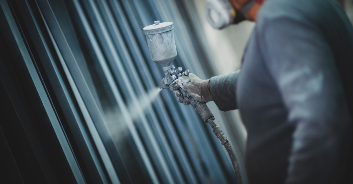 A man dressed in blue is spraying a length of metal with a spray hose he’s holding in his hand.