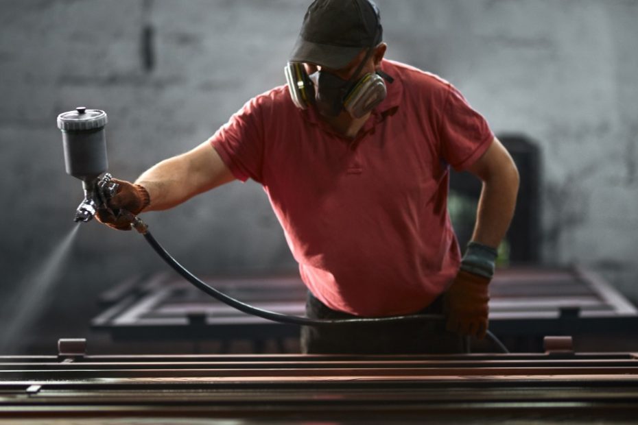 A man in a red shirt is using a spray hose to spray down some metal pieces with a mist-like substance.